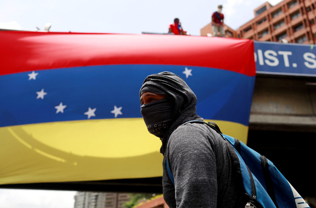 A masked demonstrator walks in front of a national flag of Venezuela during a protest against Venezuela's President Nicolas Maduro in Caracas, Venezuela July 10, 2017. REUTERS/Marco Bello