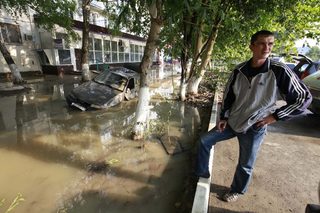 A local resident stands near a damaged car stuck in a flooded street in the town of Krymsk in Krasnodar region