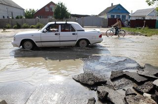 Local residents ride a car and a bicycle while moving along a flooded street in the town of Krymsk in Krasnodar region