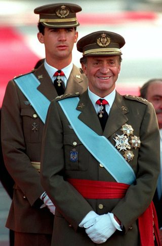 File photo of Spanish King Juan Carlos smiling in front of his son, Crown Prince Felipe, as they watch the Spanish National Day parade in central Madrid