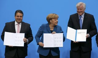 German Chancellor Merkel leader of the CDU Seehofer leader of the CSU and Gabriel leader of the SPD hold copies of a signed coalition treaty during a ceremony in Berlin