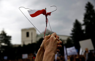 Woman holds hanger with the Polish flag attached to it as she takes part in abortion rights campaigners' demonstration "Black Protest" in front of the Parliament in Warsaw