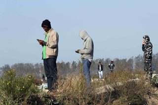 Migrants stand on high ground to get a telephone network as they use mobile phones on the eve of the evacuation and dismantlement of the camp called the "Jungle" in Calais