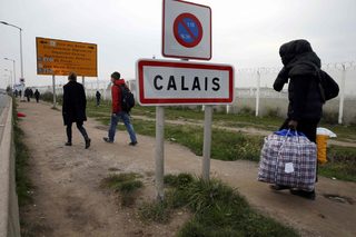 A migrant carries bags with his belongings as he walks past the Calais city limit sign on the eve of the evacuation and transfer of migrants to reception centers in France, and the dismantlement of the camp called the "Jungle" in Calais