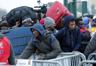 Migrants with their belongings queue near barriers at the start of their evacuation and transfer to reception centers in France, and the dismantlement of the camp called the "Jungle" in Calais
