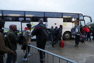 Migrants carry their belongings as they board a bus at the start of their evacuation and transfer to reception centers in France, and the dismantlement of the camp called the "Jungle" in Calais