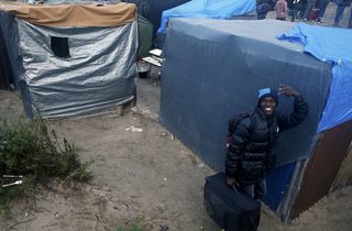 A migrant with his belongings walks past tents at the start of their evacuation and transfer to reception centers in France, and the dismantlement of the camp called the "Jungle" in Calais