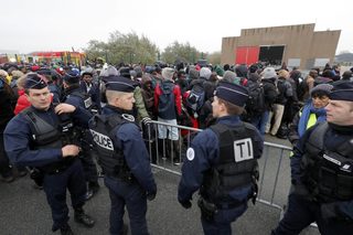 Migrants with their belongings queue near barriers at the start of their evacuation and transfer to reception centers in France, and the dismantlement of the camp called the "Jungle" in Calais
