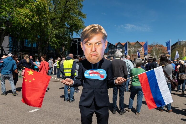 Протестиращ срещу "Алтернатива за Германия" с маска с лицето на Максимилиан Кра, държащ знамената на Китай и Русия