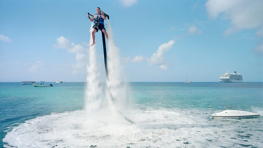 ©Паоло Уудс и Габриеле Галимберти, от проекта "The Heavens"Служител на Jetpack Cayman прави демонстрация на новия воден спорт, който вече се предлага на острова. Двигател 2000 кубика изпомпва вода през джетпака и по този начин изтласква клиента във въздуха ($359 за 30 минути). Майк Таласинос, собственикът на компанията, казва: "Джетпакът е с нулева гравитация, Кайманите са с нулеви данъци, тук сме на точното място!". Голям Кайман, Кайманови острови