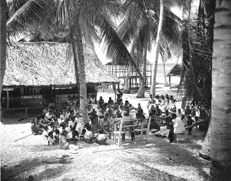 На 25 юли 1946 г. на атола Бикини САЩ извършват първия в света подводен ядрен опит. Тихоокеанският атол Бикини е известен с това, че по времето на студената война е изпитателна площадка, на която САЩ извършват в периода 1946 - 1958 година 23 експериментални взрива на ядрени и водородни бомби.<br /><br />На снимката: Местните  жители на атола Бикини са се събрали на открито за последната им църковна служба, преди да бъдат прехвърлени от американската флота на атола Ронгерик, на 109 мили.<br />