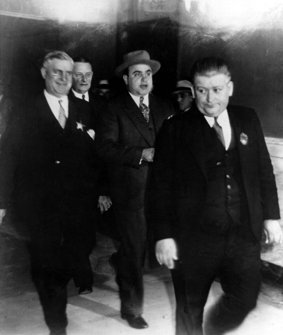На 13 март 1931г. е свикано тайно заседание на федералното Голямо жури и е разгледан искът на правителството, според който през 1924 г. Ал Капоне бил укрил данъци в размер на 32 488 долара.<br />
<br />
На 5 юни 1931 г. голямото жури е свикано отново и излиза с 22 обвинения срещу Капоне за укриване на данъци в общ размер от над 200 000 долара. Седмица по-късно е издаден трети обвинителен акт въз основа на доказателствата, събрани от Нес и неговия екип. Капоне и 68 членове на неговата организация са обвинени в около 5000 отделни нарушения на забраната за алкохол, някои от които датирали от 1922 г. Обвиненията по злоупотребата с данъци имали предимство пред нарушенията по забраната.<br />
<br />
На снимката: Ал Капоне напуска съдебната зала в Чикаго  под стража след заседание на 24 октомври 1931 г.