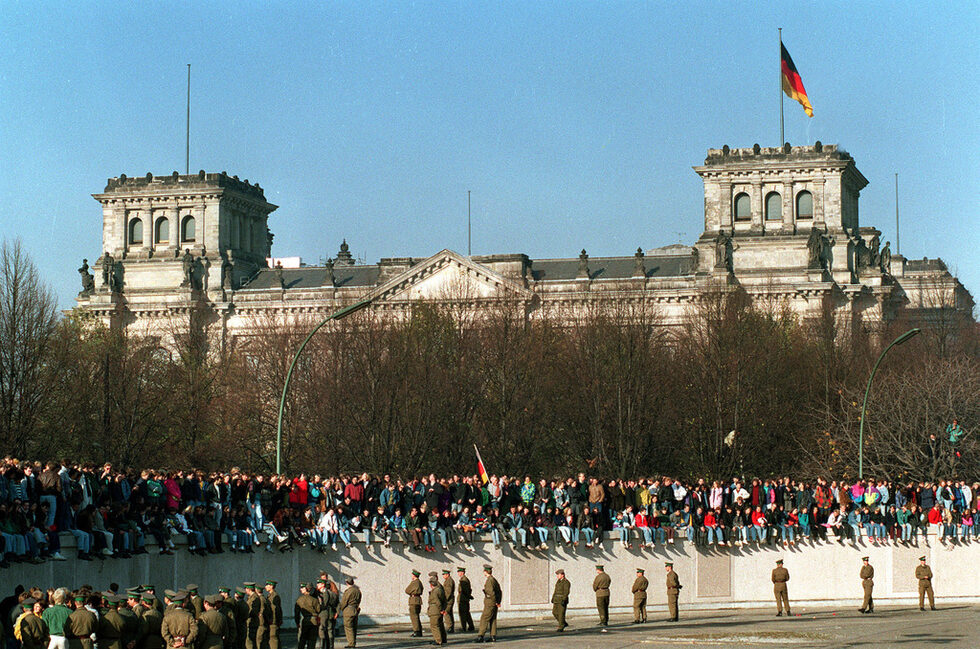 10 ноември 1989 г. - ден след падането на стената, германци седят върху нея пред Райхстага. Ден по-рано източногерманските власти са обявили облекчаване на режима за посещения във Федерална република Германия.