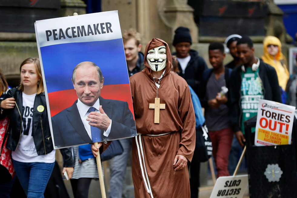 Мъж с маска държи знаме с лицето на Владимир Путин на протест в деня на откриването на Конференцията на Консервативната партия в Манчестър.<br />