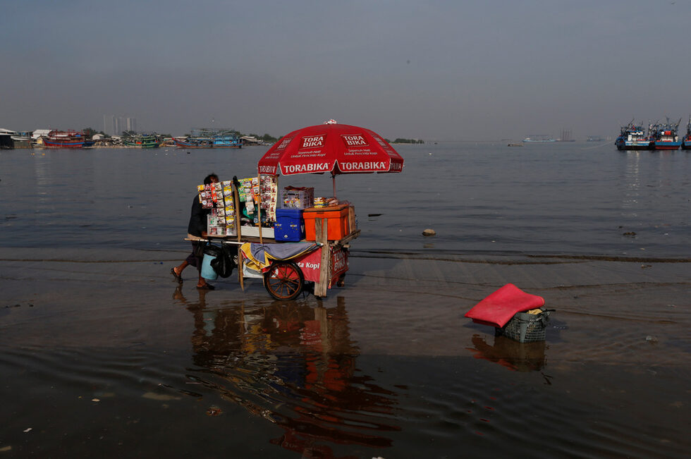 Уличен търговец бута количка с храни, по залятия с вода кей на пристанище Кали Адем в Джакарта