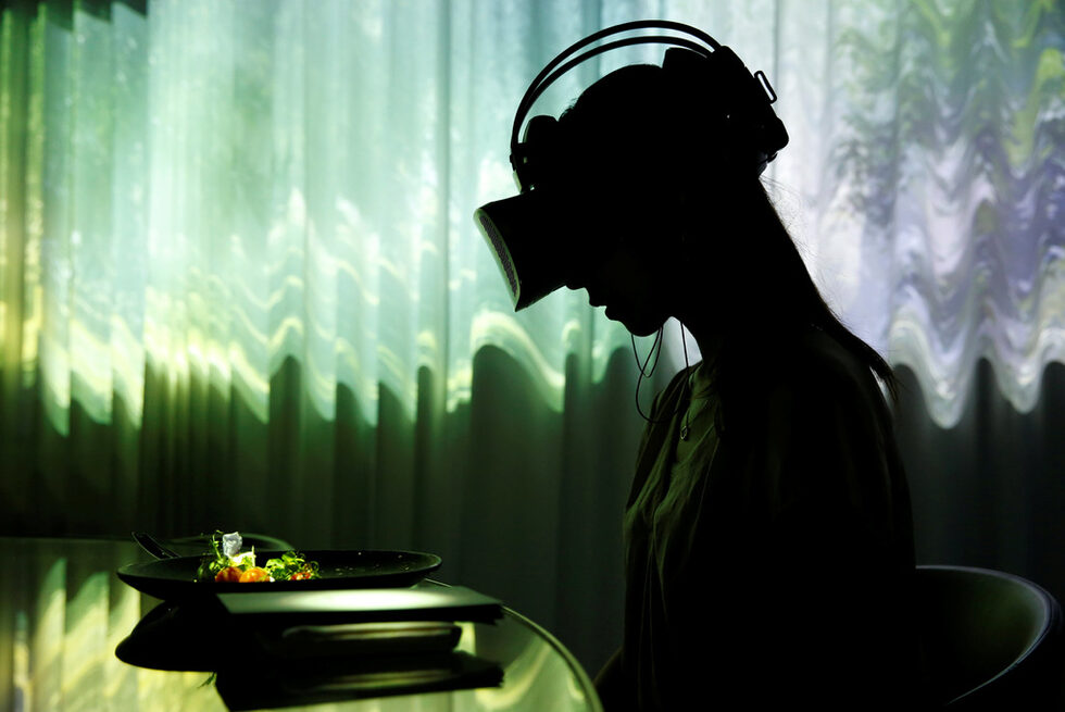 Жена с VR очила седи на маса по време на представянето за медиите на ресторант "TREE BY NAKED, yoyogi park" в Токио, Япония. Той включва виртуална реалност, прожекция и музика. Целта е да се подобри удоволствието на вечерята от храната.