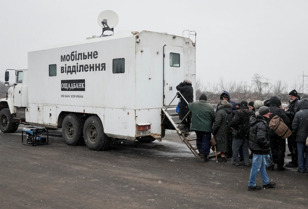 Служители на държавна банка пътуват с бронирани автомобили до пункт, където жителите и от двете страни на разломната линия могат да теглят пари.