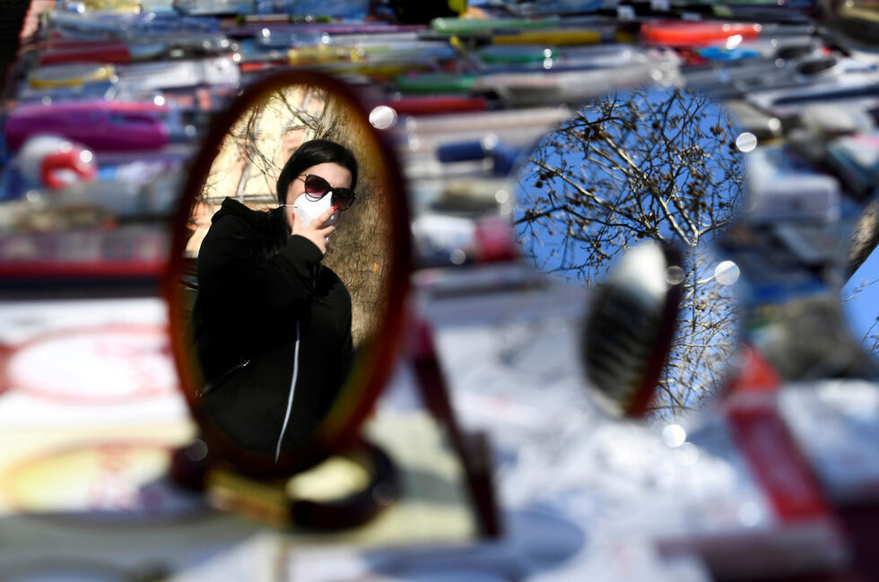 Жена, носеща защитна маска, се отразява в огледало на пазар на втория ден от безпрецедентното блокиране на цяла Италия, наложено с цел забавяне на огнището на коронавирус, в Милано.