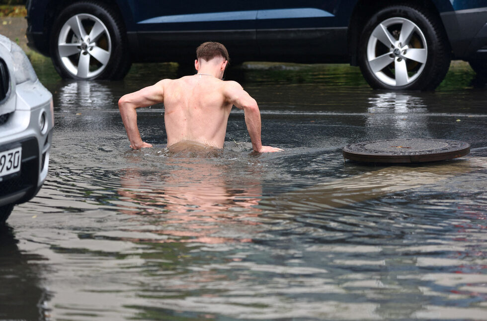 Човек скача в дупка, пълна с дъждовна вода, на наводнена улица по време на проливни дъждове в Берлин, Германия.