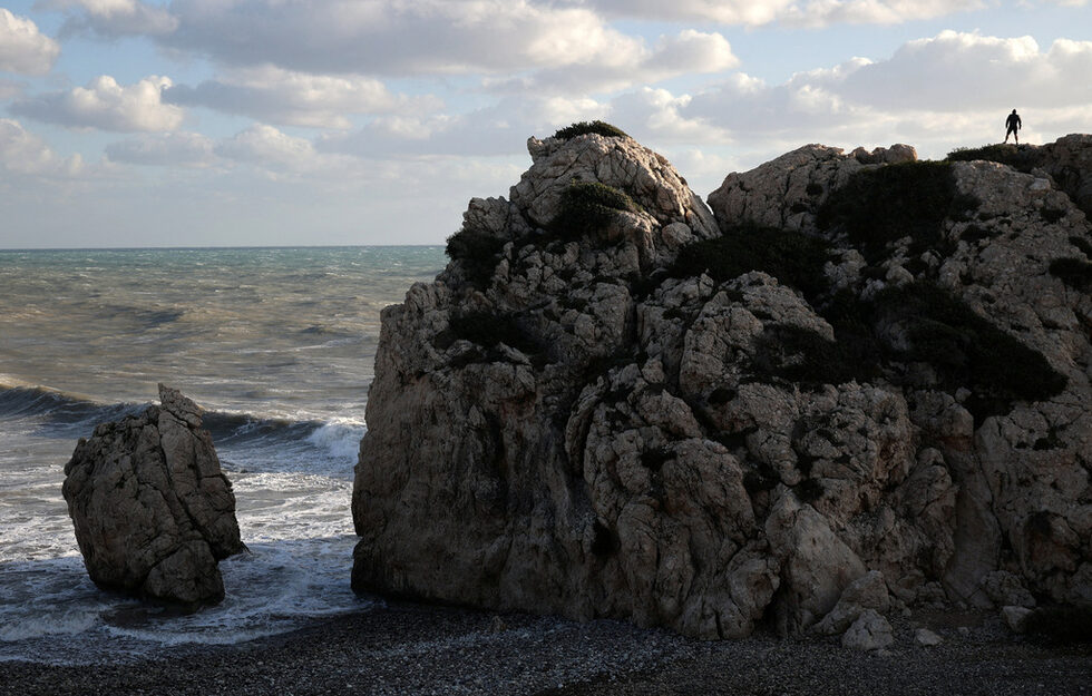 Мъж стои на плажа Petra tou Romiou (Камъкът на Ромиос), който според мита е родното място на Афродита, древногръцката богиня на любовта и красотата, близо до Пафос, Кипър.