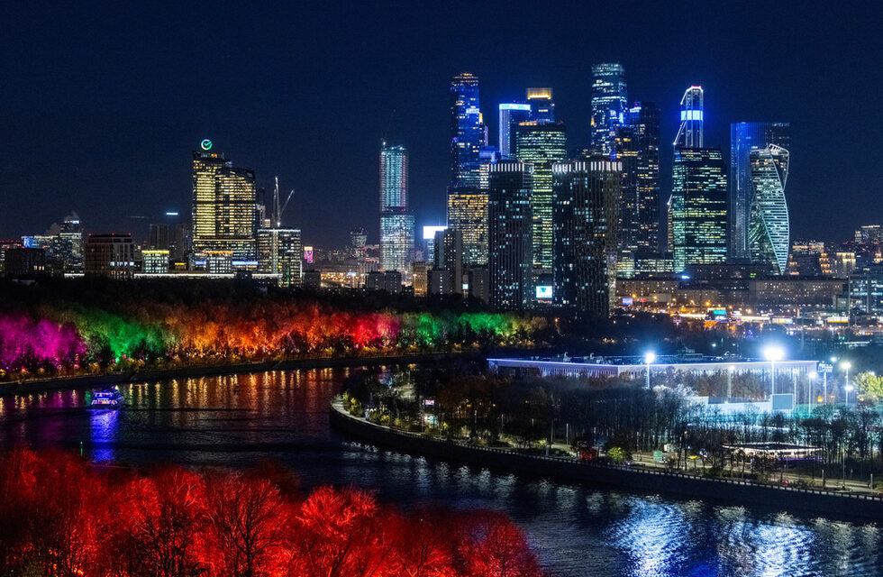 Изглед към Международния бизнес район "Москва сити" и река Москва, чийто бряг е осветен с разноцветни светлини.