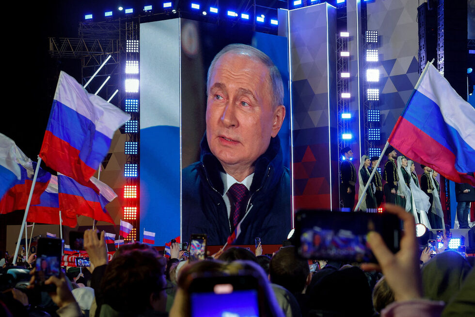 В Русия, където противниците на президента Владимир Путин са цензурирани и хвърляни в затвора, Путин спечели убедително вота, с което още повече затвърди властта си.<br /><br />На снимката: Руският президент Владимир Путин, който беше обявен за победител в президентските избори от избирателната комисия на страната, се вижда на екран на сцената на митинг, посветен на 10-годишнината от анексирането на Крим от Украйна, на Червения площад в центъра на Москва