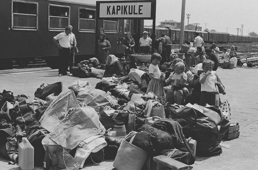 В първите дни на юни 1989 г. хиляди български турци напускат страната, принудени от репресивната политика на тоталитарната власт, а драматичното събитие е цинично назовано "голямата екскурзия". Наред с другото позорно клише ("възродителен процес"), създадено няколко години по-рано, за да обозначи насилствената смяна на имената.<br /><br />Изложбата <a href="https://www.dnevnik.bg/bulgaria/2025/06/08/4791259_progonvaneto_na_sunarodnicite_turci_ili_za_pametta_i/" target="_blank">"Прогонването"</a> е малка част от <a href="https://assimilationarchive.com" target="_blank">"Визуален архив на асимилацията"</a>, представяща фотографиите на Сюлейман Акман (роден в България) и Бехич Гюналан (роден в Истанбул), които са запечатали драматични моменти от събитията, протичали в различно време - в годините 1951, 1969, 1985, 1989, но с едно и също трагично внушение: хора - българи и турци - които са живели в съседски сговор и взаимопомощ, се разделят принудително заради порочната насилствена същина на политическия режим. <em>Още по темата <a href="https://www.dnevnik.bg/bulgaria/2025/06/08/4791259_progonvaneto_na_sunarodnicite_turci_ili_za_pametta_i/" target="_blank">тук</a>.</em><br /><br />На снимката: Юни, 1989 г. Капъкуле - Одрин. Децата и възрастните чакат уреждането на документите, с което се занимават младите, за да потеглят към неизвестността.